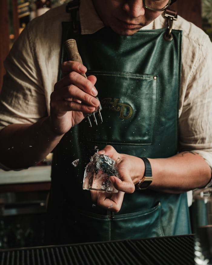 Close-up of a bartender using an ice pick to carve ice, creating a refreshing drink charm.