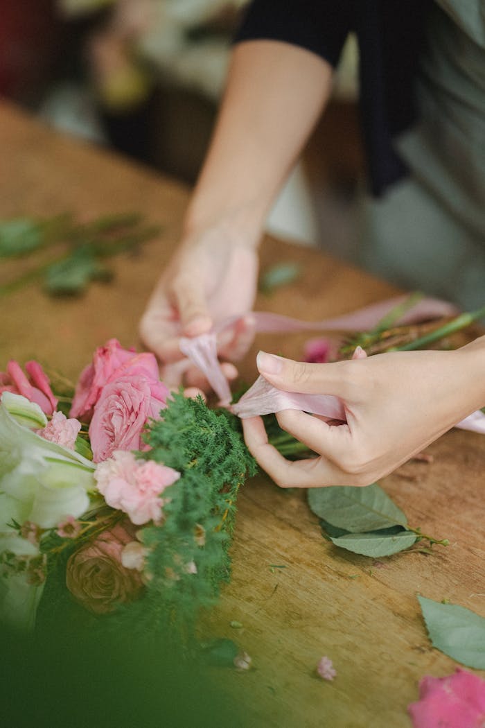 A florist's hands skillfully arranging a delicate flower bouquet with vibrant pink roses.